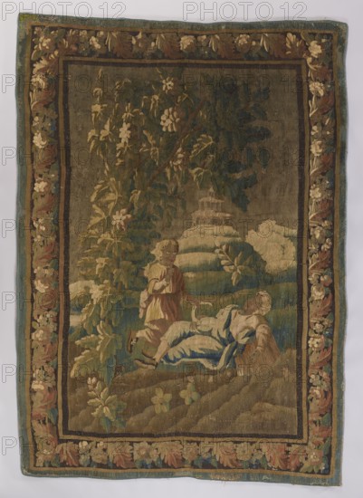 Figural tapestry; flowers, floral ornaments, pastoral scenes, fabrics, interior furnishings, decorative tapestries, interior decorations, borders. In the center foreground, under a tree, a sleeping girl holds a sickle; above her, a young boy kneels, raising a finger to his lips. In the background is a building with a double conical roof and a distant horizon. Border with floral motifs. Colors: brown, green, and sand. 2nd half of the 18th century, France. Materials: fabric. Height 280 cm; width 195 cm., A woven scene on a rectangular textile shows a large central panel with a landscape and two human figures surrounded by a decorative floral border. The border contains a repeating floral and leaf motif in shades of brown, beige, green, blue, and muted gold against a darker ground. Inside, the scene uses earthy tones with a muted greenish-brown background, darker green foliage, and touches of pale beige and cream for flowers and highlights. In the foreground a reclining figure draped in p...