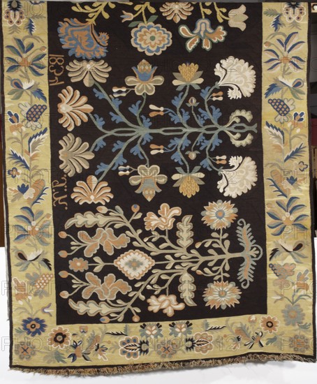 Court rug, woven signature and date at upper edge: JK1834, 1834., Poland. Fabrics; weaving. Height 186 cm, width 416 cm. The central field is filled with motifs of four stylized trees with flowers and leaves, generally fanciful; only the carnation flowers are recognizable. Surrounded by a single-strand border with motifs of stylized flowers, fruit, and leaves arranged in a tendril. Colors: main field background black; borders sandy yellow; ornament in blue, greenish, dirty yellow, sapphire blue, and white. Plant and floral motifs; decorative interior furnishing., A woven textile with a dark background and a pale yellow border, decorated overall with a symmetrical arrangement of stylized floral and foliate motifs. The central dark field contains a few branching stems rendered in muted green and blue, supporting several large, rounded flowers and blossoms in shades of cream, beige, pale blue, soft orange, and light gold, along with smaller buds and leaf shapes in similar colors. The pale...