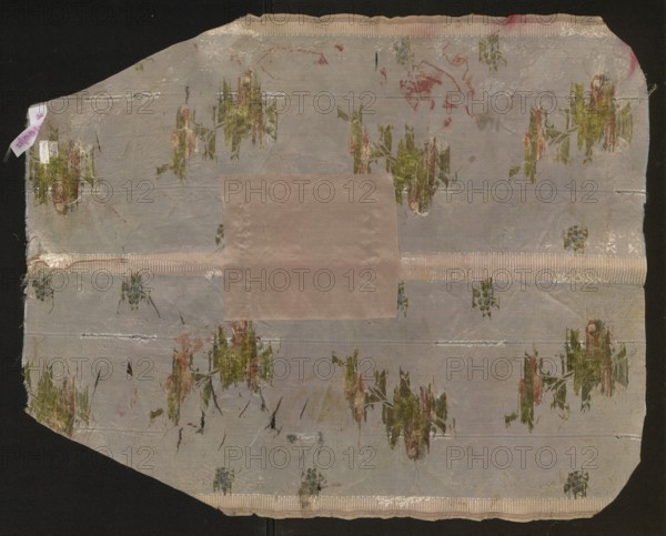 Fabric fragment, fragments of silk fabrics, patterned fabrics, fragments of a larger textile object, fragments of unsewn liturgical garments, 18th-century French silk fabrics with floral and plant patterns, fabrics with preserved selvedge, preserved pile width, and preserved repeat. Blue-pink brocaded and embroidered grosgrain. Pattern created by thicker and thinner embroidered stripes, a lace ribbon winding in the background brocaded with white weft, and larger and smaller bouquets of roses brocaded with colored wefts. Colors: pink-blue background blue and pink warp. Brocading: white, celadon, pale green, pale anguere, brownish-brown, grass green. Warp embellishments: white, blue, graphite. Sub-weft embellished with white weft. Width of selvedge edge 0.7 cm; width of the piece 54 cm; repeat 54 x 38.5 cm. 18th century, France. Height 67 cm, width 54 cm., A worn rectangular piece of fabric with uneven edges lies against a dark background, showing a muted pale gray base with a central sq...