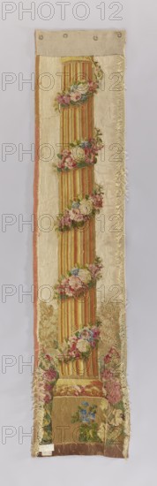 Ornamental tapestry, flowers, leaves, floral ornaments, columns, fabrics, interior decorations, interior furnishings, decorative fabrics. The column is identical to those flanking the pastoral scene in the tapestry inventory no. SZT 2211. Identical colors: cream, red, pink, green, and yellow. 1750–1780, France. Medium: fabrics. Height 225 cm, width 48 cm., A long vertical textile panel with a central fluted column motif in warm yellow and orange tones, wrapped at intervals with garlands of flowers in pink, red, blue, and green; the column sits on a square plinth in muted brown and gold hues surrounded by more floral clusters. The background fabric is a pale cream color with a narrow border on one side in faded pink and a fringed edge on the other side; the panel shows areas of wear and fraying along the edges and surface. At the top a plain linen or canvas strip in beige with round metal rings is attached, and the bottom edge shows a darker brown strip of fabric. Overall colors visible...