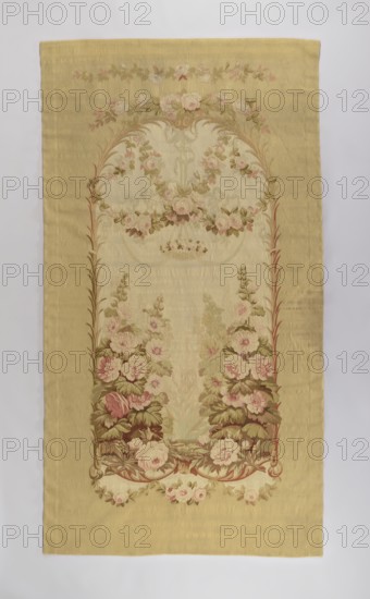 Ornamental tapestry, flowers, floral ornaments, interior decorations, fabrics, decorative tapestries, interior furnishings. In the center, an arcade built of palm branches; on the sides, tall flowering hollyhocks; at the top, rose garlands. No border. Colors: light green, white, and pink. Early 19th century, Aubusson. Fabrics. Height 290 cm, width 158 cm., A rectangular textile with a muted yellow-beige background featuring an ornate vertical floral design; a central arched panel filled with garlands and clusters of roses in shades of pale pink and cream with green and olive leaves, framed by stylized brown and reddish-brown stems, and surrounded by a plain yellow-beige border; additional small floral swags in pink and cream accent the top and bottom edges; overall colors visible include yellow-beige, pale pink, cream, green, olive, brown, and reddish-brown.