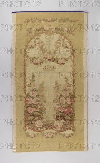 Ornamental tapestry, early 19th century, Aubusson. In the center an arcade built of palm branches; on the sides tall flowering hollyhocks; at the top rose garlands. No border. Colors: light green, white, and pink. Materials: fabric. Dimensions: height 290 cm, width 158 cm., A rectangular textile with a beige background and a narrow off-white border, decorated with a vertical oval arch of floral embroidery. The embroidery shows a group of roses and leafy vines in shades of pink, pale rose, and muted red, with leaves in various greens and brownish-green tones. The arch is framed by slender brownish stems and surrounded by additional floral sprays in pale pink and green. The overall palette includes beige, off-white, pink, green, brown, muted red, and a small visible trim of blue along the top edge.