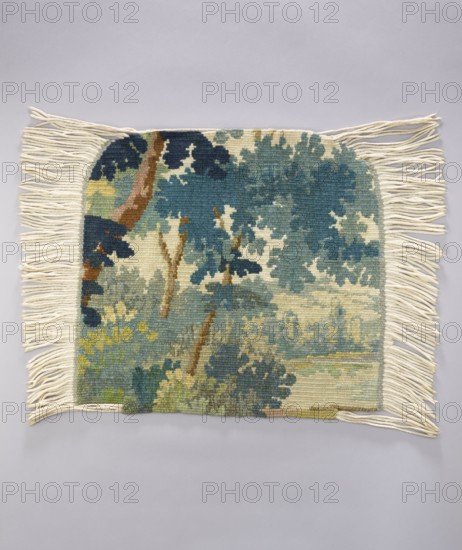 Tapestry chair cover, Repossession provenance. Depicts leaves, trees, landscapes, castle buildings on the right, tall trees on the left. Decorative fabrics for interior furnishings. Colors: green, blue, and white. 1st half of the 20th century, Vienna. Materials: fabrics. Height 53 cm; width 62 cm., A rectangular woven textile with cream fringe along the shorter sides lies flat on a pale gray background; the woven area shows a landscape scene in muted blues, teals, greens, cream, brown, and touches of yellow, with tree-like shapes, rounded foliage forms, and vertical trunk-like elements, the weave texture visible and the fringe strands spread outward on both sides.