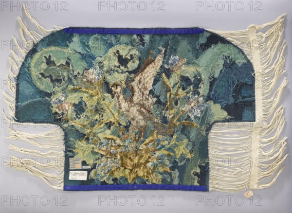 Tapestry coverings, repossession provenance. Subject: leaves, birds, fabrics, borders, interior decorations, interior furnishings, decorative fabrics. Details: a seat—a bird with spread wings among large leaves and flowers; b backrest—flowers among large leaves. Colors: green, blue, yellow, ochre, and brown. Date: 1st half of the 20th century. Place of origin: Vienna. Material: fabrics. Dimensions: height 74 cm, width 109 cm., A woven textile with fringed edges laid flat on a light background, showing a central area of mixed, textured threads forming an abstract floral or organic cluster with loose ends and shaggy surface; the main woven field includes rounded shapes and layered patterns. The visible colors include shades of blue, teal, turquoise, dark navy, pale green, cream, beige, brown, mustard yellow, and touches of white and purple. Cream-colored fringe extends from the sides and bottom, and a narrow strip of deep purple fabric runs along the top and bottom edges. A small tag-lik...