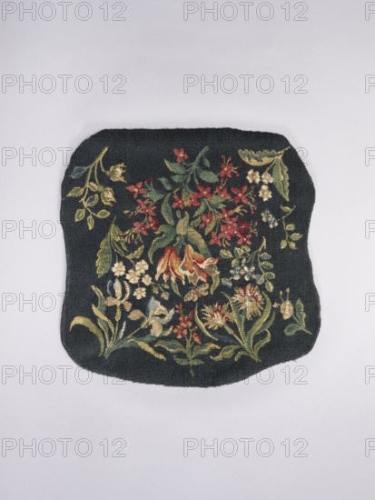 Tapestry covering, Design: leaves, floral ornaments, fabrics, interior decorations, interior furnishings, decorative fabrics, flowers, floral bouquets, tapestries. a Seat: bouquet of lily of the valley in the center with sprigs of other flowers around, including tulips. b Backrest: lily flowers in the center with sprigs of other flowers around, including irises. Colors: dark green. Date: 1st half of the 20th century. Place of origin: Vienna. Materials: fabrics. Dimensions: height 68 cm, width 72 cm., A dark rectangular textile with rounded corners lies flat against a pale background, featuring an embroidered floral design in shades of green, red, yellow, cream, and blue; the embroidery shows a cluster of leaves and various stylized flowers with elongated stems and petals, including several red blossoms, a few cream and yellow blooms, and green foliage interwoven across the dark field, with edges of the textile appearing slightly irregular and frayed.