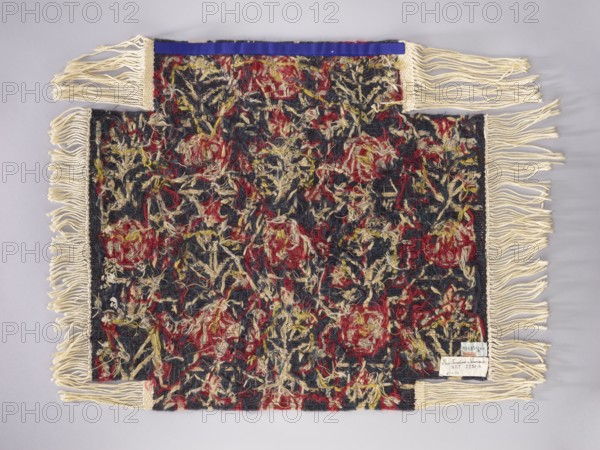 Tapestry covering with stylized flower trees identical on the seat and backrest; floral ornaments, borders, and decorative fabrics; navy blue background with red, yellow, and cream ornamentation. Fabric, 1st half of the 20th century, Vienna; height 67 cm, width 74 cm., A rectangular woven textile with fringed edges displayed flat against a light gray background, showing a dense, textured surface of tangled yarns in dark blue, red, cream, and touches of yellow; the main field has an irregular, mottled pattern of these colors with loose, curly yarns creating a shaggy appearance, and cream-colored fringe extends from the shorter sides and from two small protruding tabs, while a narrow band of blue trim appears along one of the shorter edges.
