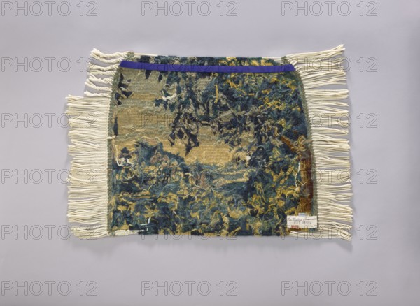 Tapestry covering, flowers, leaves, floral ornaments, fabrics, interior decorations, decorative fabrics, interior furnishings, furniture upholstery; a seat: forest landscape with a thicket of leaves; b landscape with a view of a mountain with a castle. Colors: green, blue and yellow. 1st half of the 20th century, Vienna. Fabrics. Height 72 cm, width 79 cm., A rectangular woven textile with a rough, tufted surface in a mix of blues, greens, yellows, and beige sits flat against a pale gray background; it has long cream-colored fringe along the shorter sides, a narrow band of solid deep purple across the top edge, and a small stitched patch near one corner; the woven area shows irregular, dense clusters of yarn and loose fibers in dark blue, teal, olive green, mustard yellow, and beige, with some areas of exposed base weave in lighter beige and muted green.