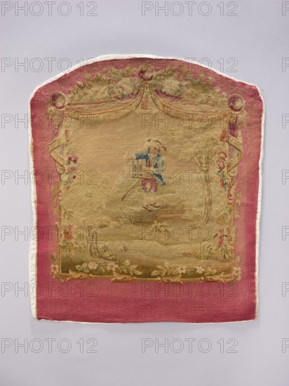 Tapestry covering depicting floral ornaments and boys in pastoral scenes, draperies suspended above and flowers around; figure wearing a tailcoat. Materials: fabrics. Colors: cream, pink, sky blue, ochre, beige, light green, and red. Date: post–mid-18th century. Possible origins: Aubusson or Beauvais. Dimensions: height 69 cm, width 57 cm. Provenance unknown., A rectangular textile with a rounded top sits against a pale gray background; the textile has a wide deep pink border and a central scene woven in muted beige, green, blue, and pink tones; the central area shows a pastoral motif with a small figure wearing blue and pink near the middle, a tree to the right, and floral and leafy decorations along the edges and bottom; the top of the central scene features draped garlands and round ornamental shapes in green and pink; the overall fabric shows woven texture and areas of faded color with visible stitching along the outer edge in an off-white color.