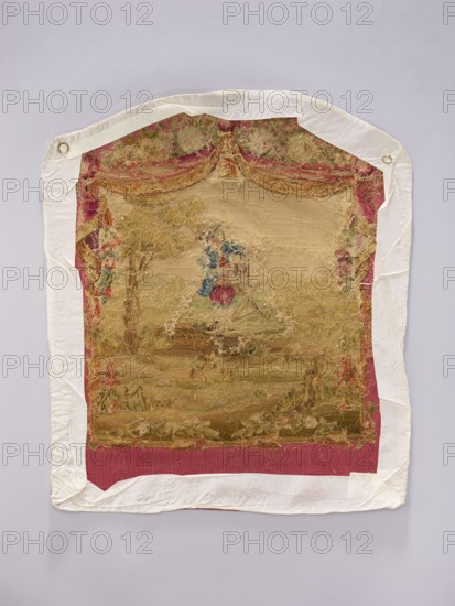 Tapestry covering, Design: flowers, floral ornaments, boys, pastoral scene with draperies suspended above and flowers around; figure wearing a tailcoat. Materials: fabrics. Colors: cream, pink, sky blue, ochre, beige, light green, and red. Date: post–mid-18th century. Possible origins: Aubusson or Beauvais. Dimensions: height 69 cm, width 57 cm. Provenance unknown., A worn rectangular textile with a rounded top is displayed against a pale gray background; the textile shows a central faded scene in beige and tan with traces of blue and red in the middle, surrounded by frayed areas and loose threads in yellowed beige and brown, a decorative border in deep pink and muted red, and a white fabric facing folded over the edges with visible metal rings at the upper corners.