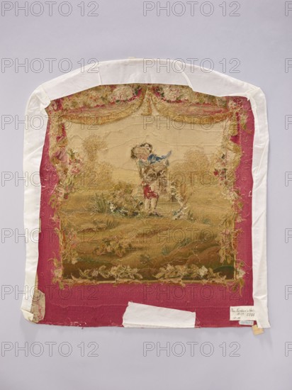Tapestry covering, creator unknown, provenance, floral ornaments, boys, pastoral scenes; fabrics, interior decorations, interior furnishings, decorative fabrics, flowers, tapestries, gobelins, furniture upholstery; draperies suspended at the top and flowers around. Colors: beige, cream, pink, blue, and red. After the mid-18th century. Possibly Beauvais or Aubusson. Fabric. Height 69 cm, width 59 cm., A worn rectangular textile with a scalloped top edge is mounted on a pale background; the textile has a deep pink border and a central faded scene in beige and brown tones showing a small figure wearing a blue garment standing amid grassy, tangled vegetation, surrounded by frayed decorative edges in muted gold and green; white fabric strips are affixed around the outer edges and a small white patch is attached near the bottom, with areas of loose threads and visible wear throughout.