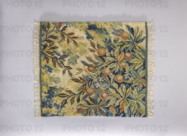Tapestry chair cover, Repossession provenance. Design: flowers, leaves, trees, landscapes; fruit and flower decorations. Use: interior decoration/furnishing, furniture upholstery, tapestry. Materials: fabrics, tapestry. Colors: cream background with green, yellow-orange, brown, and yellow ornamentation. Date: 1st half of the 20th century. Place of origin: Vienna. Dimensions: height 76 cm, width 67 cm., A rectangular woven textile with fringed short edges lies flat against a pale gray background; the textile shows a dense botanical pattern of leaves and round fruit-like shapes in a palette of green, blue, yellow, beige, brown, and rust tones, with darker blue and green outlines and accents, and lighter cream and tan areas creating a mottled backdrop, and a narrow darker border running along the right edge.