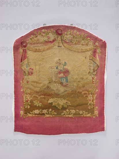 Tapestry covering, provenance, decorative tapestry with flowers, leaves, floral ornaments, girls, boys, and pastoral scenes; used for fabrics, interior decorations, furniture upholstery; design includes hanging draperies at the top and flowers around. Colors: beige, cream, green, sky blue, ochre, and red. Post–mid-18th century. Possibly Beauvais or Aubusson origin. Height 71 cm, width 58 cm., A rectangular textile with a rounded top hangs against a pale gray background; it has a wide pink border and a central woven scene in faded beige, tan, green, blue, and pink tones. The top of the textile features draped curtain-like shapes in beige and pink with floral garlands in green and pale pink, and a round decorative element at the apex. Within the central area a small figure wearing pink and blue sits near a pedestal or column, surrounded by a landscape of grassy and leafy forms in muted greens and browns. Floral garlands and leafy motifs frame the inner scene along the sides and bottom in...