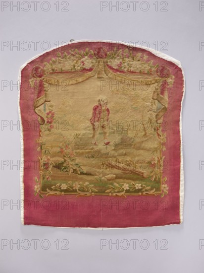 Tapestry covering, provenance, depicts flowers, leaves, floral ornaments, boys, pastoral scenes, interior furnishings and decorations, with hanging draperies at the top and flowers around. Materials: fabrics. Colors: beige, cream, ochre, green, blue, pink, and red. Date: post–mid-18th century. Possible origin: Aubusson or Beauvais. Dimensions: height 70 cm, width 58 cm., A rectangular textile with a rounded top edge features a central woven scene framed by a wide magenta border and a thin white edging; inside the border is a faded tan and beige landscape with a figure wearing a darker pink coat standing near a body of water, surrounded by muted green foliage and pale floral garlands, with decorative drapery in shades of gold and beige at the top and floral motifs in soft pinks, greens, and cream along the sides and bottom.