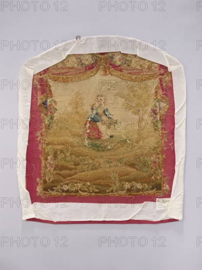 Tapestry covering, creator unknown, provenance, floral ornaments and pastoral scenes with boys; fabrics used for interior decorations, furniture upholstery, hanging draperies at the top with flowers around. Colors: beige, cream, ochre, green, blue, and red. Post–mid-18th century; possibly Aubusson or Beauvais. Height 71 cm, width 58 cm., An embroidered textile mounted on a backing is visible, with a central faded scene surrounded by decorative borders; the textile shows worn areas and loose threads, with visible colors including beige, gold, red, green, blue, pink, and white. The outer mounting fabric is white and the immediate border around the textile is a deep red; inside that border the embroidered area has a predominantly beige and gold background with accents of green and pink florals, a central figure area with touches of blue and red, and darker brown and olive tones toward the lower portion. The top edge of the textile has a curved shape and a small metal ring attached, and th...
