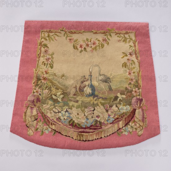 Tapestry covering, creator unknown, provenance, depicts flowers, leaves, floral ornaments, foxes, storks, boys; decorative fabric likely used as interior furnishing, tapestry or upholstery, evoking fairy-tale garden scenes with hanging draperies at the bottom and flowers around. Colors: beige, light pink, sky blue, light olive. Post–mid-18th century; possibly Aubusson or Beauvais origin. Height 57.5 cm, width 67 cm., An embroidered textile with a wide pink border surrounding a central beige field that features a decorative scene; the central area shows a group of animals near a blue and white vase, framed by floral garlands and leafy motifs in shades of green and pink; the lower portion displays a draped swag of flowers and ribbons in colors including cream, blue, purple, and gold, with tassel-like elements at the sides; overall colors visible include pink, beige, green, blue, cream, purple, gold, and hints of brown.