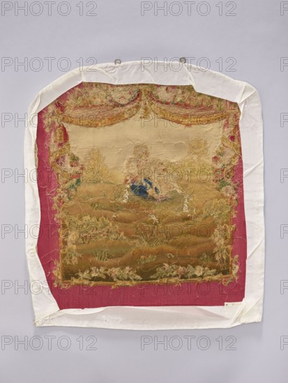 Tapestry covering, provenance, depicts flowers, floral ornaments, dogs, boys, pastoral scenes; used as interior furnishing, interior decoration, fabric for furniture upholstery; scene on grass with draperies suspended above and flowers around. Colors: beige, cream, green, ochre, blue, and red. Post–mid-18th century; possibly Aubusson or Beauvais. Fabric. Height 71 cm, width 59 cm., A rectangular textile with frayed edges is mounted on a pale background and wrapped with a white cloth border; the central fabric shows a worn tapestry scene in muted beige, tan, brown, and faded green tones with areas of loose threads in yellowish and cream hues and a small patch of dark blue; the tapestry is set against a deep pink or magenta backing visible around its edges; the white cloth border is slightly wrinkled and folded at the corners, and two metal loops are visible at the top.