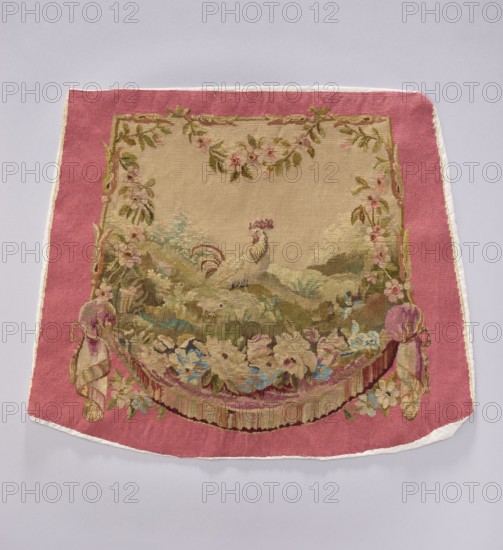 Tapestry covering, creator, flowers, leaves, floral ornaments, roosters, boys; decorative fabrics for interior furnishings and upholstery, draperies with flowers around the bottom. Colors: beige, light pink, sky blue, and olive green. After the mid-18th century. Possibly Beauvais or Aubusson origin. Height 56 cm, width 67 cm., A rectangular textile with a wide pink border and a central beige panel shows an ornate woven scene: a light-colored bird with a decorative crest stands amid a stylized landscape of green and brown hills and foliage, surrounded by floral garlands and leafy vine motifs in greens, pinks, and muted browns; the lower area features a draped swag of flowers and ribbons in shades of pink, purple, blue, cream, and green, with fringed tassel-like elements at the sides, and the outer edge trimmed with a narrow white border.
