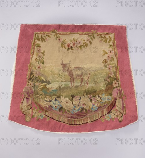 Tapestry covering, creator unknown, provenance, floral ornaments with flowers and leaves; oxen and boys; interior decorations and furnishings including tapestries, decorative fabrics, gobelins, furniture upholstery, and draperies with flowers at the bottom. Colors: beige, pink, sky blue, ochre, and olive. Post–mid-18th century; possibly Beauvais or Aubusson. Materials: fabrics. Dimensions: height 57 cm, width 68 cm., A rectangular woven textile with a wide pink border surrounds a central beige panel depicting a pastoral scene; the central area shows a light brown animal standing on grassy terrain with muted green and tan hills behind it, framed at the top and sides by garlands of leaves and flowers in shades of green, pink, and pale yellow. The lower edge of the central scene features a curved floral swag with a mix of soft blue, cream, pink, and green flowers and foliage, and draped tassel-like elements in pink and beige at the lower corners. The outer border is solid rose-pink, and t...