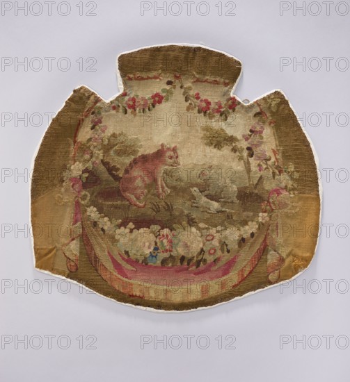 Tapestry armchair seat cover, unknown provenance. Design: flowers, floral ornaments, hares, foxes; draperies at the bottom with flowers around., tapestry, upholstery fabric; decorative fabrics, interior furnishings. Colors: beige, brown, ochre, pink, red, blue. Date: post–mid-18th century. Possible origin: Aubusson, Beauvais . Dimensions: height 58 cm, width 61 cm., An ornate textile fragment with a rounded, shield-like outline shows a central pastoral scene rendered in muted tones of brown, tan, pink, green, cream, and hints of blue; a pinkish-brown cat sits on a grassy patch facing a small light-colored bird near the water, surrounded by a garland of flowers and foliage in shades of pink, cream, green, and red; a draped ribbon-like swath in pink and cream runs along the lower edge, framing a cluster of mixed blossoms, while the outer areas of the textile display worn brown and tan backgrounds with areas of lighter beige and subtle green, and the whole piece is set against a pale gray...