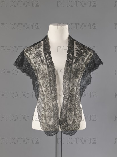 Mantilla, floral ornaments; Chantilly lace; lace; clothing accessory; women's clothing; fashion; mantillas; triangular with highly raised upper corners; 2nd half of the 19th century; France; height 36 cm, A white mannequin torso against a gray background wears a delicate black lace shawl or collar with a floral pattern; the lace drapes over the shoulders and down the front in two panels edged with scalloped trim, showing intricate openwork and layered motifs that create a contrast between the sheer black lace and the solid white of the mannequin.