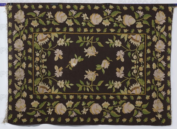 Kilim, Boncza fl. ca. 1920–1930. In the main field, symmetrically presented motifs of floral branches: four around the center and four in the corners. The wide border is decorated with arranged floral branches and two rows of single leaves surrounding them. Colors: background — brown; ornament — yellow, straw, and green. 1920s. Poland, Tomczyce. Woven fabric kilim, height 207 cm, width 150 cm., A rectangular woven textile with a dark brown background featuring a repeating floral pattern in shades of pale pink, cream, light yellow, and green; a central rectangular field contains scattered stylized flowers and leaves, surrounded by a narrow framed border and a wider outer border of continuous floral garlands and small leaf motifs; the flowers appear in rounded and bell shapes with accompanying leafy stems; the colors visible include dark brown, pale pink, cream, light yellow, various greens, and small areas of tan; the edges show frayed fringe on one side and small fabric tabs or clips a...