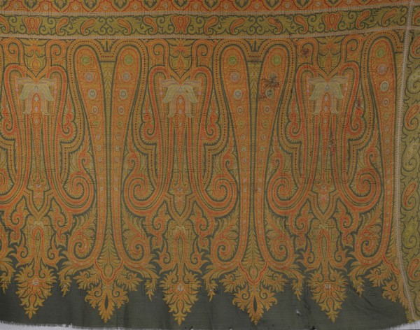 Fragment of a cashmere shawl. Its ending features two types of stylized palmette motifs, some similar to a double bota. It is surrounded on three sides by a narrow border with a leafy tendril motif, and at the bottom by another band with an arcade motif. Likely a product of Kashmiri workshops. 19th century, India. Materials: cashmere; function: clothing/accessory shawl. Dimensions: length 78.5 cm, width 143 cm., A patterned textile showing a repeating ornate paisley-like design with sweeping curved teardrop shapes and scrolls, featuring a few large floral motifs integrated into the paisley forms and a decorative narrow border along the top edge; the main field has a dark background while the pattern is rendered in shades of orange, yellow, green, and touches of pale blue and pink, with dense small dot and line detailing creating an overall intricate, stitched appearance.