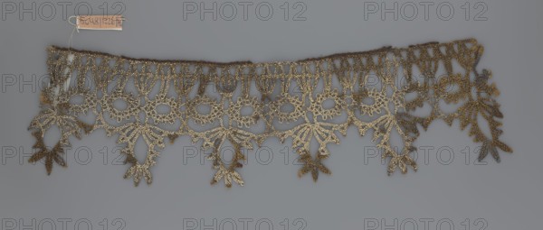 Lace, bobbin lace, 16th/17th century, Flanders, fabric, width 7 cm, length 27 cm, A decorative lace trim with an openwork floral and leaf pattern laid flat against a neutral gray background, showing a scalloped lower edge formed by hanging leaf-like motifs and a straight upper edge with looped stitching; the lace appears metallic with gold and bronze tones, and there are areas that show darker brown and muted gray shades.
