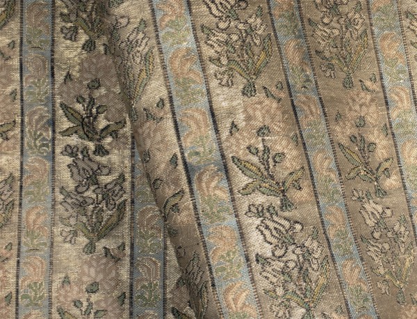 Fabric fragment. Gold-plated silk with a motif of irises and carnations in vertical stripes. Floral sprigs arranged in an alternating rhythm, turning first to the left irises and then to the right carnations. In narrower stripes, miniature stylized red flowers tulips?. Weave structure: compound weft. Prominent wefts: gold thread with braiding, light and dark green, light and dark pink salmon, blue, white, black. Colors: gold background weft weave; pattern colors green, pink-salmon, blue, black tied in weft weave. Main warp: dark yellow; main weft: cream. Dimensions of fragment: 8.0 x 4.3 cm; edge width: 0.5 cm. Selection width: 0.5 cm, fabric report: 4.3 x 8 cm. 18th century, Iran. Overall dimensions: height 54 cm, width 28 cm., A textured fabric with a striped pattern featuring a few vertical bands in beige and light blue, decorated with floral and leafy motifs in muted green, dark green, and brown; the background shows varying shades of tan and cream with subtle shimmer, and the wove...
