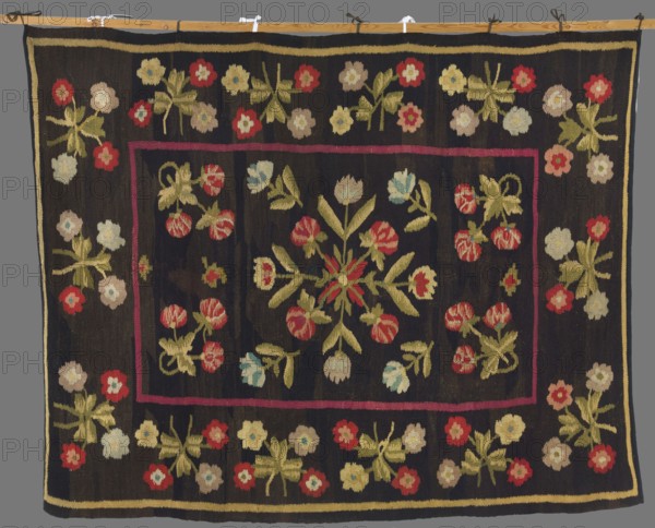 Kilim, 19th century, Poland. Wool fabric, height 214 cm, width 167 cm. In the center is a rhomboidal rosette made of simple flower sprigs, surrounded by projections of flower sprigs; four bouquets occupy the corners. The wide border is decorated with floral bouquet motifs. Background dark brown; ornament in red, pink, blue, and lilac., A rectangular textile with a dark background featuring a central rectangular field outlined in a thin reddish border and filled with floral motifs; the design includes a central symmetrical floral cluster with elongated green leaves and red-pink, pale blue, and cream blossoms, surrounded by several smaller floral sprays in similar colors. Around the central field is a wide dark border decorated with repeating floral clusters composed of green leaves and flowers in red, cream, pale blue, and light beige, with a narrow pale yellow outer edge. The overall color palette includes dark background tones, green, red, pink, pale blue, cream, beige, yellow, and to...