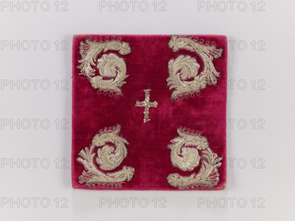 Pall, palls, church paraments, revindication provenance, plant ornaments, 19th century, Europe, liturgical parament, height 20 cm, width 20 cm, A square fabric panel in deep magenta with a plush texture rests on a light gray background, featuring a small cross-shaped cluster of shiny sequins near the center and four ornate metallic appliqué motifs placed near each corner; the appliqués have a metallic gold color with intricate swirling leaf-like shapes and small looped accents, and the piece shows subtle variations in the magenta pile where the light hits.