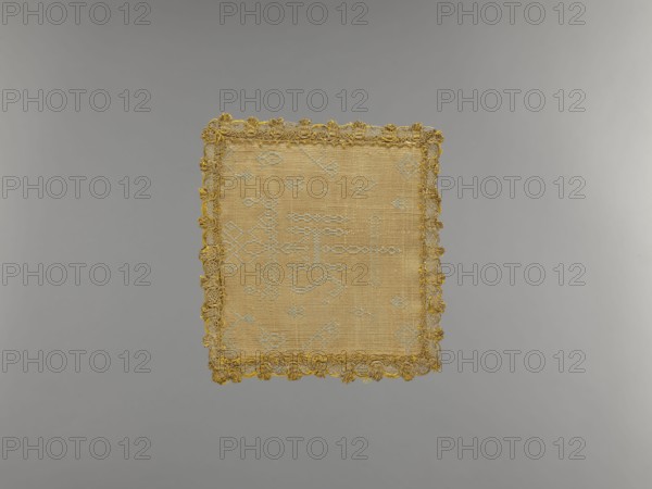 Palka, origin, church paraments; crosses; monograms; plant ornaments; sacred art; churches and chapels furnishings; 17th century, Europe; liturgical parament; height 13 cm; width 12 cm, A square textile with a woven center in beige and pale blue tones is shown against a neutral gray background; the textile has a yellow-gold decorative trim with looped fringe around its edges, and the woven area displays pale blue geometric motifs on a beige field.