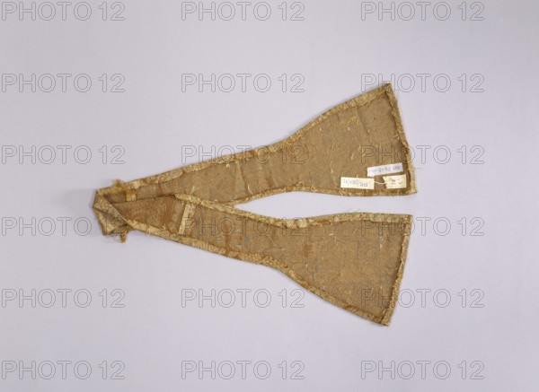 author, church paraments, liturgical vestments, plant ornaments, sacred art, churches and chapels furnishings, 18th century, France, Lyon, liturgical vestments, length 90 cm, width 16 cm, A fabric object in shades of gold and tan lies flat against a light gray background; the textile has a woven texture with visible frayed edges and loose threads, and a few areas show subtle greenish and pale yellow accents; the piece consists of two tapered sections joined at one end, forming a V-like shape, and the edges are finished with a narrow gold trim that appears slightly worn.