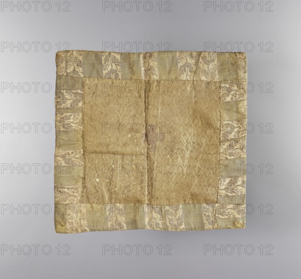 Velum; unknown author; liturgical parament; church paraments; flowers and plant ornaments; sacred art; churches and chapels furnishings; 18th century; Russia; height 32.5 cm; width 30.5 cm, A square textile laid flat with a central panel of worn, patterned fabric in shades of gold and tan, bordered by a band of fabric with a repeating leafy motif in pale green, cream, and muted gold; the central area shows a subtle diamond-like woven pattern and some irregular darker spots and creases, while the border displays alternating vertical segments of pale green and cream with the leaf pattern, all set against a neutral gray background.