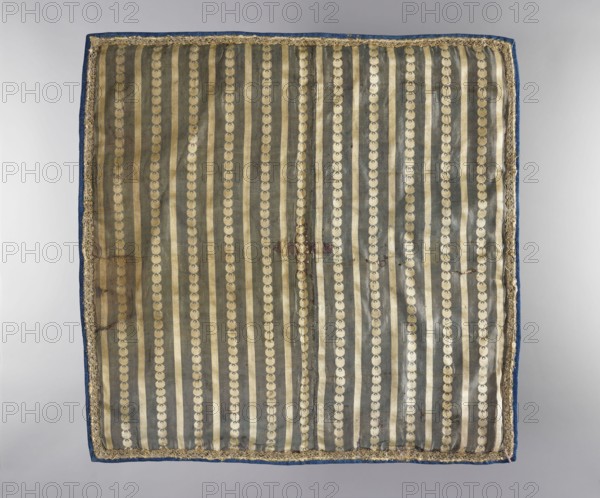 Velum, church paraments, revindication provenance, plant ornaments, flowers, sacred art, churches and chapels furnishings, 18th/19th century, Turkey, liturgical parament, height 46 cm, width 46.5 cm, A square textile with vertical striped pattern, showing alternating darker gray-green and lighter beige-gold stripes, each lighter stripe punctuated by a series of circular motifs in a pale gold tone; the textile has a narrow decorative trim along its edges in a muted gold color and is backed or edged with a blue fabric; the surface shows slight wrinkles and a few small darker stains, and the overall background behind the textile is a neutral light gray.
