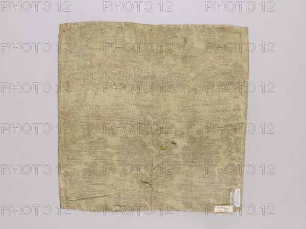 Velum, vellum, church paraments, reclaimed, 19th century, Europe, liturgical parament, height 47 cm, width 47 cm, A square piece of fabric laid flat against a pale background, showing a textured, slightly wrinkled surface with an overall light yellowish-beige color and areas of muted grayish-beige shading; the fabric has subtle woven patterns visible across it and a few small darker spots and tiny imperfection areas; the edges are slightly irregular and the lower edge shows a small folded corner.