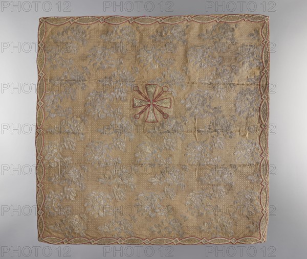 Velum; unknown creator; gift; church paraments; plant ornaments; sacred art; churches and chapels furnishings; 18th century, France; fabric; liturgical parament; height 50 cm; width 50 cm, A square textile with a tan background covered in a repeating floral pattern in a pale silvery-gray, featuring a central emblem outlined in red with pale gold interior details, and a decorative border with interlacing shapes in red and gold; visible creases and slight irregularities in the fabric surface.