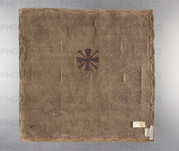 Velum; unknown creator; ; church paraments; plant ornaments; sacred art; churches and chapels furnishings; 18th century; France; fabric; liturgical parament; height 50 cm; width 50 cm, A square piece of fabric with a worn beige-brown ground and a decorative scalloped border in golden and reddish tones, showing a central dark brown emblem with radiating petal-like shapes and small round ends; the surface has scattered areas of metallic embroidery in faded gold and silver hues and visible patches of wear and thinning; the edges show a few small tags and remnants attached, and the overall palette includes beige, brown, gold, silver, and hints of red.