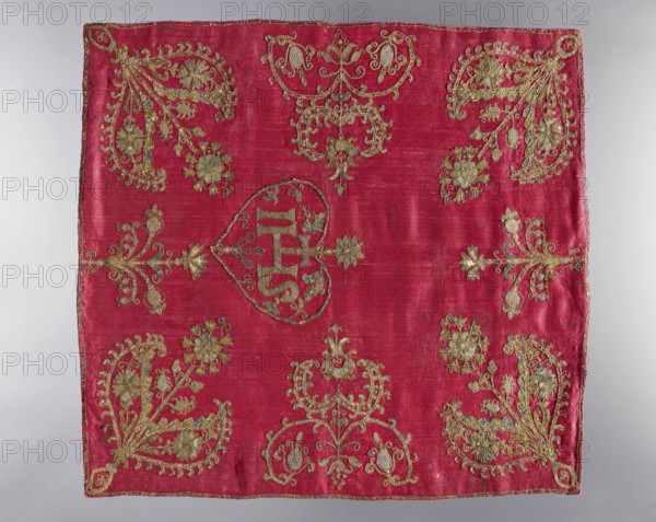 Velum, revindication provenance, church vestments, embroidery, flowers, leaves, plant ornaments, sacred art, churches and chapels furnishings. Velum sewn from scarlet satin, embroidered with silk yarn and metal threads. In the center, a heart-shaped medallion features the letters IHS and a cross, with stylized floral sprigs on the sides. In the corners and along the sides are varied stylized flower bushes. The edges are trimmed with narrow gold braid. The lining is made of silk fabric brocaded with motifs of twigs and flowers and fruit growing from them on a light background. 18th century, Poland, liturgical vestment, height 49 cm, width 52 cm, A square textile with a deep red background embroidered with metallic gold thread in ornate floral and foliate motifs; a group of heart-shaped and scroll-like embroidered designs sit near the center and corners, with several stylized flowers and leaf sprays arranged symmetrically around the piece; the gold embroidery includes raised, textured st...