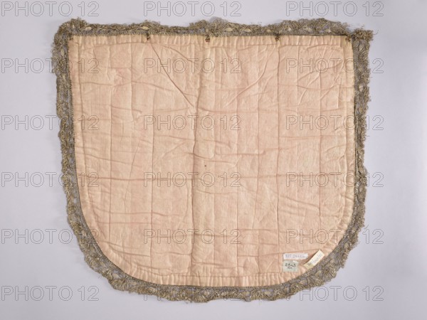 A hood from a church cope. The hood of the liturgical cope is made of navy blue silk with appliquéd decoration of stylized flowers, leaves, and stars. In the lower center, under the bishop's hat, is a cartouche with the Odrowaz Dolega coat of arms. Predominant colors: gold, silver, green, and brick red. Trimmed with contemporary metal lace braid. The appliqué was transferred to a new fabric. 18th century, Poland. Materials: fabrics. Height 58 cm, width 61 cm., A rectangular fabric panel with a rounded bottom edge is visible, mostly pale pink in color and showing many creases and stitched quilt-like lines; it is edged with a decorative fringe in a metallic grayish-gold tone that forms an irregular border around the fabric.