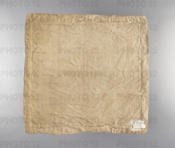 Velum. Velum made of blue silk fabric. In the center is an applied radiant medallion with the IHS monogram with a cross and a burning heart. In the corners and in the center of each side are traces of torn-out applied flower sprigs. Trimmed with wide silver braid. Linen lining. 18th century, Poland. Liturgical vestment. Height 45 cm, width 46.5 cm., A square piece of fabric with a wrinkled texture fills the image, showing a woven pattern and stitched hems along the edges; the cloth is a beige to light tan color with subtle darker and lighter areas from creases and wear, and there is a small pale patch near one corner that appears lighter than the surrounding fabric.
