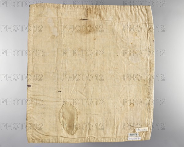 Velum; unknown creator; church parament; revindication provenance; flowers and plant ornaments; sacred art; churches and chapels furnishings; 18th century, Italy; liturgical parament; height 46 cm, width 51 cm, A rectangular piece of fabric laid flat with visible wrinkles and seams, primarily beige to light tan in color with areas of slightly darker staining and small dark spots; a rounded patch of similar but slightly shinier beige fabric is sewn near the lower left area, and there are a few small darker marks and tiny holes scattered across the surface; the edges show stitched hems and faint discoloration, and a small group of paper tags is attached near the lower right edge but their text is ignored.