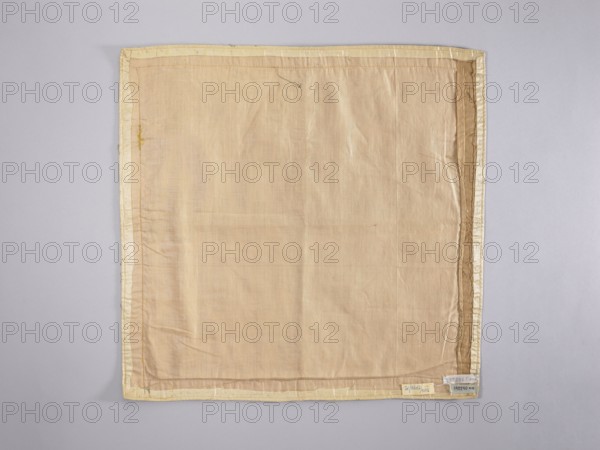 Velum;, Church vestment, early 18th century, Poland. Silver lamé velum embroidered at corners and along edges with colorful floral branches green, pink, salmon pink, beige; floral motifs, flowers, leaves, plant ornaments. At the bottom center a gold equal-armed cross is applied. Edges trimmed with galloon; cotton lining. Liturgical vestment. Height 50 cm, width 50 cm., A flat textile square laid against a neutral background, showing a central panel of light beige fabric with visible weave and subtle creases, surrounded by a narrow pale yellow border and a slightly darker beige trim; the fabric has a few faint irregular folds and small loose threads along the edges, and the overall color palette includes beige, pale yellow, light brown, and the soft gray of the backdrop.