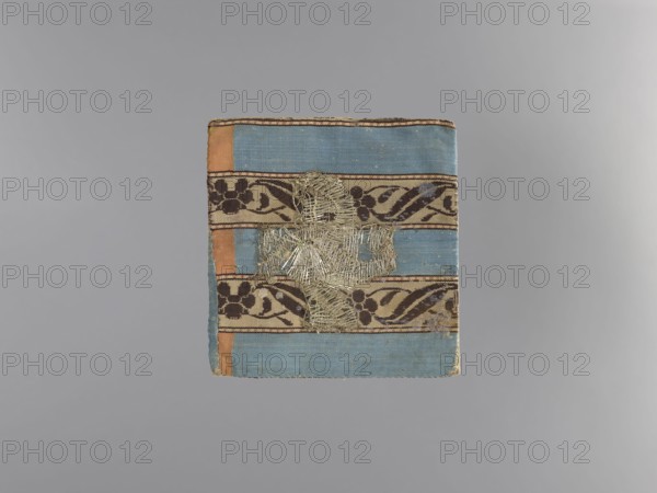 18th century; liturgical parament church parament with flowers and plant ornaments; sacred art; churches and chapels furnishings; height 13 cm, width 13 cm., A rectangular textile with horizontal bands in blue and tan, accented by vertical orange strips at the sides, featuring decorative dark brown floral and vine patterns on the tan bands, with a central area of frayed metallic threads forming an irregular cross-like shape; the textile shows worn edges and small areas of discoloration against a neutral gray background.