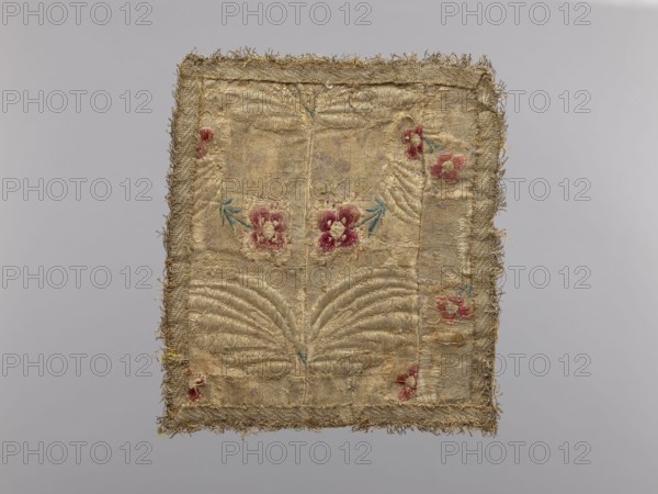Pall, church paraments, unknown origin, flowers, leaves, plant ornaments, sacred art, churches and chapels furnishings, 18th century, France, liturgical parament, height 19 cm, width 17 cm, A rectangular textile with frayed edges displayed against a pale gray background shows a worn beige or tan fabric base with a decorative border in a similar golden beige hue; the central area features embroidered floral motifs in pink and faded red with small accents of teal or blue-green for leaves, and there are raised quilted or padded stitched patterns creating symmetrical fan-like shapes; the textile surface appears aged with areas of discoloration and threadbare spots, and the fringe around the perimeter is a mix of beige and golden tones.