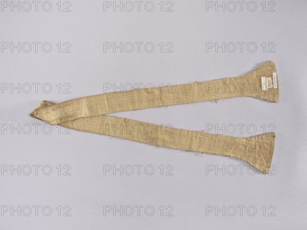 Stole, church paraments; silk stole embroidered with carnation sprig motifs; flowers, leaves, plant ornaments; liturgical vestment for churches and chapels; sacred art; ca. 1750, Poland; length 177 cm, width 14.5 6.5 cm., A long, narrow fabric strip with a tapered, flared end is laid out against a light gray background; the fabric appears beige to light tan with visible weave texture, slight wrinkles, loose threads, and some uneven edges, and a few small darker spots and areas of discoloration are visible along its surface.