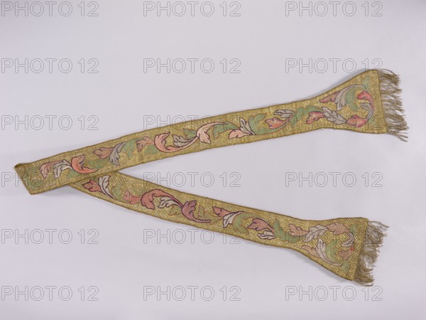 Stole, church paraments; flowers; liturgical vestments; plant ornaments; sacred art; churches and chapels furnishings. Stole embroidered with a leafy twig motif in silver, green, and two shades of pink. Gold fringe sewn to the ends of the paddles. See manipular inventory number SZT 2449. 17th/18th century, Poland. Liturgical vestment. Length 212 cm, width 19 cm., A long decorative textile laid flat in a diagonal arrangement with a few fringed ends, showing an embroidered scrolling leaf-and-flower pattern; the textile has a dominant gold background with visible areas of pink, green, pale blue, and muted purple in the ornamental motifs, and the fringes appear goldish-beige.