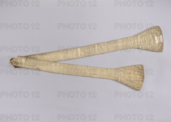 Stole, church paraments, flowers, leaves, liturgical vestment; white silk stole embroidered with a pattern of floral sprigs, without a distinct composition; fabric probably cut from a larger piece. Equal-armed crosses made of gold lace are sewn into the center of the stole's pallettes and waistband. The edges of the pallettes are trimmed with the same lace. 18th century, Poland; liturgical vestment; length 205 cm, width 18 9 cm., A long, narrow fabric strip with widened paddle-like ends lies diagonally across a pale gray background; the fabric appears to be a muted gold or beige color with a subtle sheen and visible weave texture, showing slight wrinkles and folds, and a small portion of a different-colored lining peeks out at one folded end.