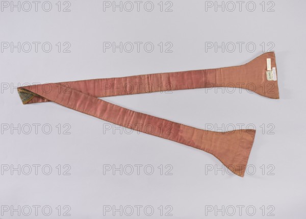 Stole, church paraments, flowers, leaves, liturgical vestments, plant ornaments, sacred art, churches and chapels furnishings, 18th century, place of origin unknown, liturgical vestments, length 196 cm, width 20 7 cm, A long, narrow fabric strip laid diagonally across a light background, appearing in a muted pinkish-rose color with subtle darker and lighter variations in the weave; the strip widens at both ends into flattened, paddle-like shapes and one end is folded to reveal an interior with a small section of blue-green patterned fabric and a thin gold trim; the edges of the pink fabric show a fine dark stitching or border.