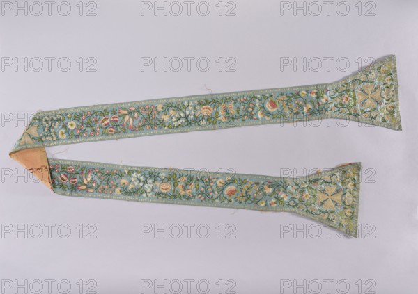 Stole, church paraments, liturgical vestment, floral ornaments, sacred art, churches and chapels furnishings, Basilica of the Holy Sepulcher Jerusalem. The stole is made of blue satin, embroidered with a floral tendril motif. In the center of each paddle and on the center waistband are embroidered equal-armed gold crosses. Pink silk lining bears the printed inscription LONGITUDO SANCTISSIMI SEPULCHRI DOMINI NOSTRI GESU CHRISTI, stylized flower bushes, and representations of architecture temple in Jerusalem?. A card is attached to the stole with ink text describing it as a stole of the Tomb of Christ in Jerusalem on blue satin, embroidered with flowers, pink lining with the inscription, and noting it was sent by the Latin Patriarch in Jerusalem in 1828 to Fr. Tomasz de Nowina Nowin, Biblical Bishop of Jerusalem, General of the Canons Regular of the Tomb of Christ. The Latin Patriarch then was Francesco Maria Fenzi 1738–1829. Tomasz Nowinski 1746–1830 — last General of the Order of the H...