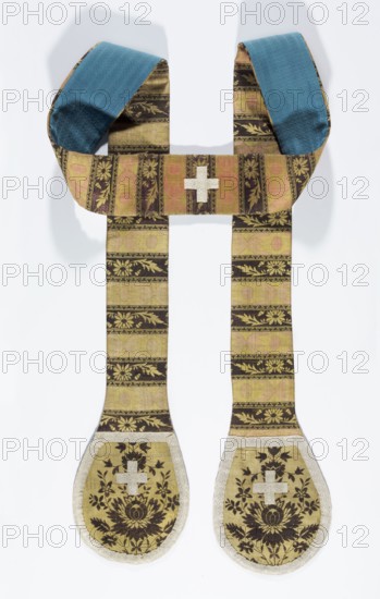 Stole made from a kontusz sash, Poland; 2nd half of the 19th century with 18th-century, Oval ends palletes trimmed with narrow white cotton braid—cut from the heads of the sash so the center of each pallete is composed of flower heads from flower bushes. Horizontal stripes alternate with floral tendrils and strap motifs in the reserves. Colors: brown for the flowers and pattern backgrounds with tendrils; yellow and salmon for the backgrounds of the heads and shelves with the straps. Lined with blue cotton damask. Kontusz sash origin, floral and strap ornament; liturgical vestment. Length 154 cm, width 16 cm., A long ornamental fabric piece resembling a looped scarf with two long hanging bands, displaying a patterned weave in shades of gold, brown, and muted pink, with a textured blue underside at the curved top ends; the hanging bands show alternating horizontal stripes and floral motifs in gold and dark brown, ending in rounded teardrop-shaped panels bordered in pale trim that contain...